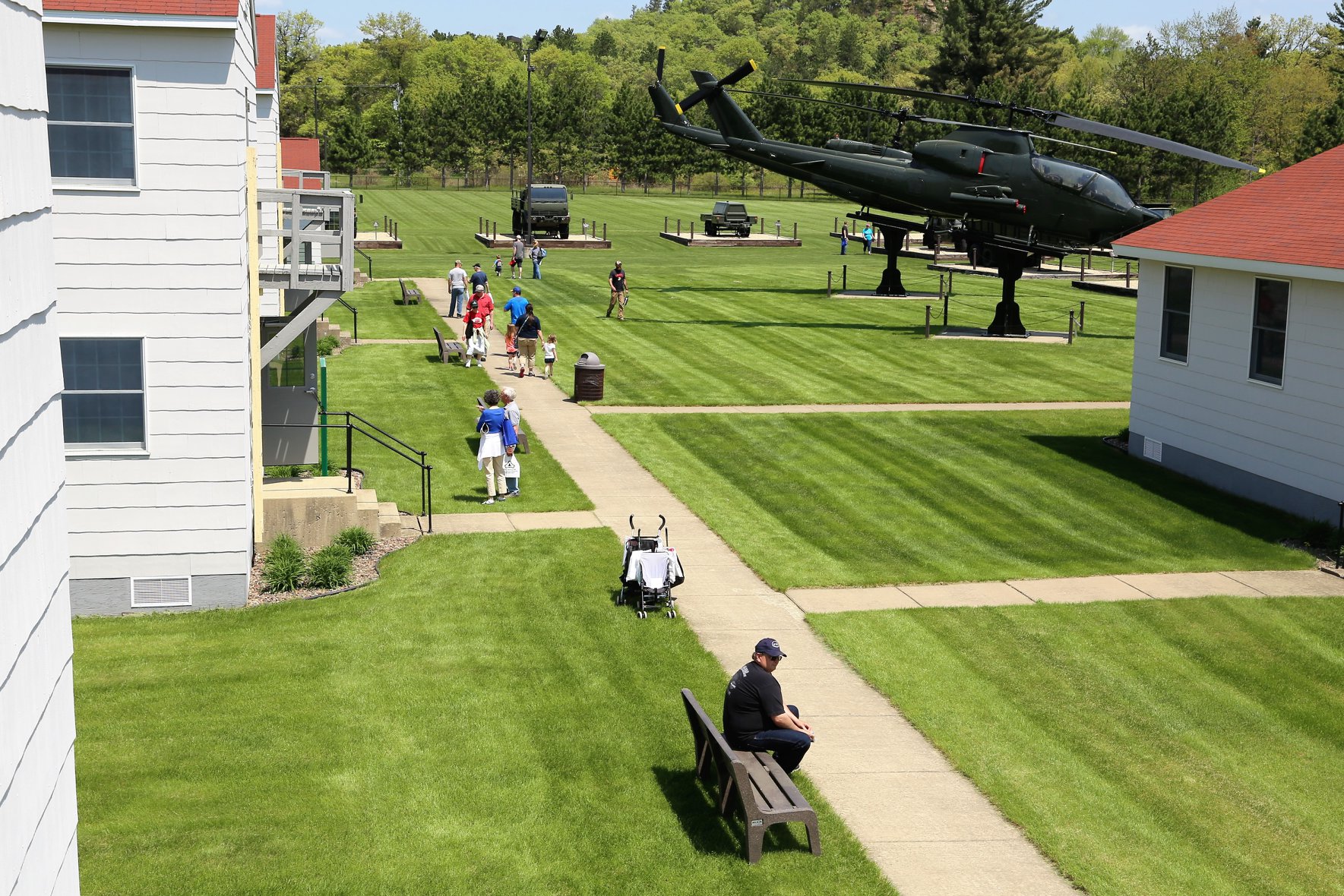 Outside of Fort McCoy's Historical Center with several people walking along a sidewalk on a sunny day.